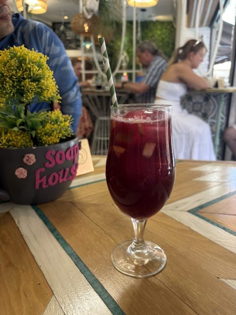 Tall glass of red sangria with fruit and a striped paper straw on an inlaid patterned wood table, cafe interior and other diners behind