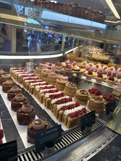 Patisserie display case packed with rows of pastries and tarts, a small card labelled St Antoine at the front
