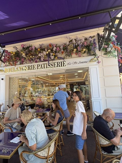 Boulangerie Patisserie Le St Antoine storefront under a purple awning, dried flowers above the sign, people seated at rattan chairs outside