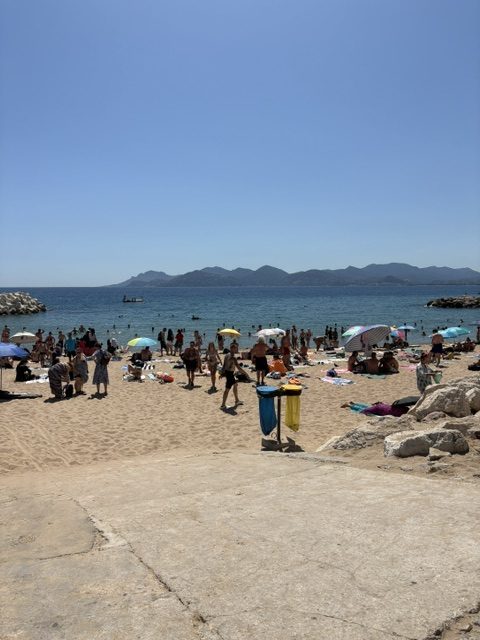 Sandy beach crowded with swimmers, towels and umbrellas, blue sea and a mountain headland across the bay