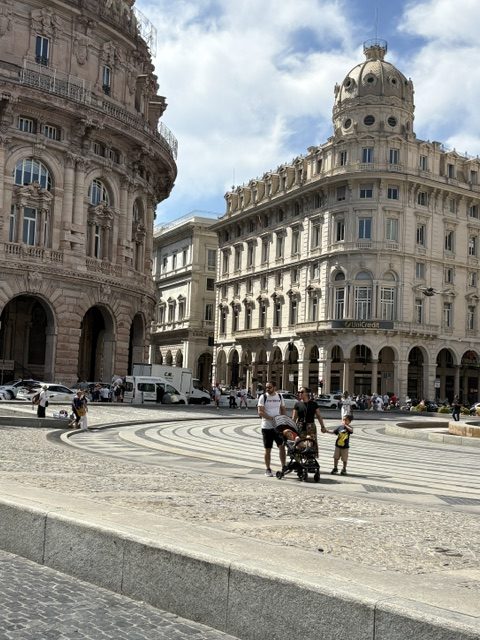 Grand domed and arcaded palazzi around a wide paved piazza, family with a stroller crossing the curved steps