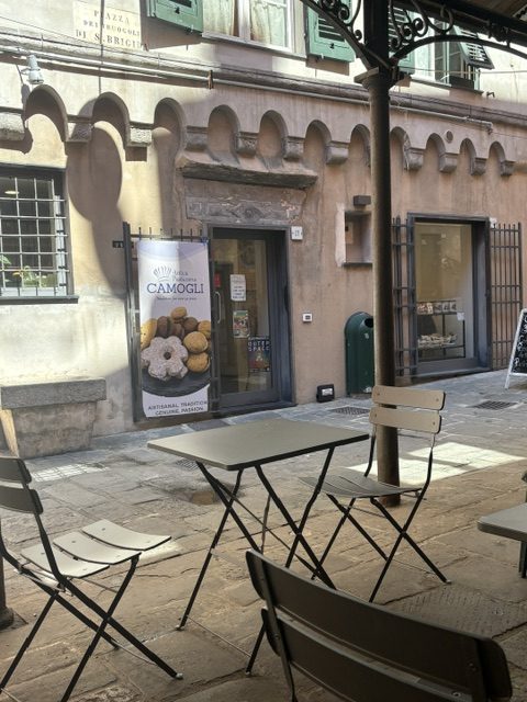 Empty folding bistro tables and chairs in a narrow alley outside a pastry shop with a Camogli banner