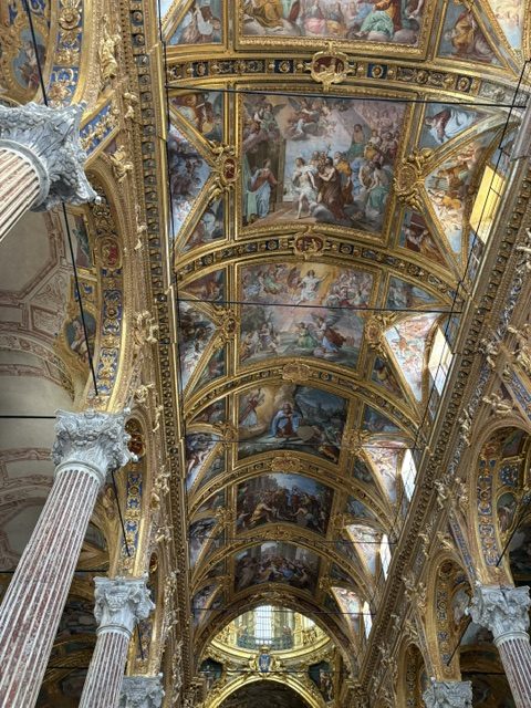 Frescoed and heavily gilded vaulted ceiling with painted panels, marble column capital in the foreground