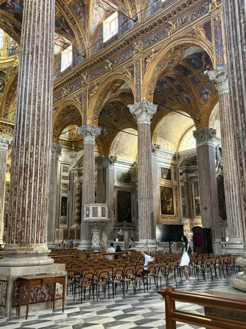 Nave columns and arcade with rows of wooden chairs below, one visitor in white