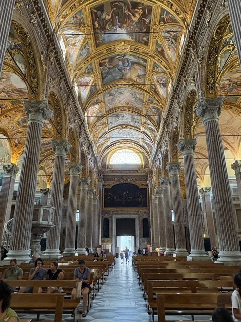 Full-length view down the church nave with pews both sides, marble columns, gilded frescoed ceiling