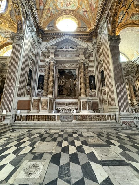 Ornate marble high altar beneath a domed lantern, checkerboard marble floor in foreground