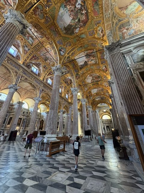 Church side aisle with several visitors walking, gilded frescoed ceiling and tall fluted columns