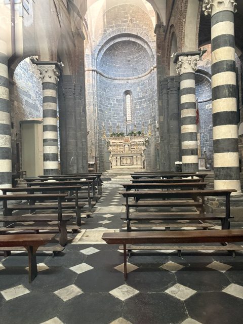 Older stone church interior with black-and-white striped columns, wooden benches, stone apse and altar