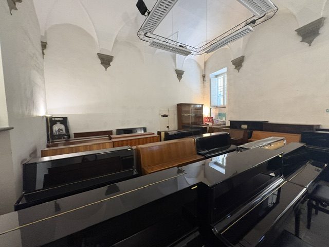 Rows of upright and grand pianos filling a white vaulted hall in a music store