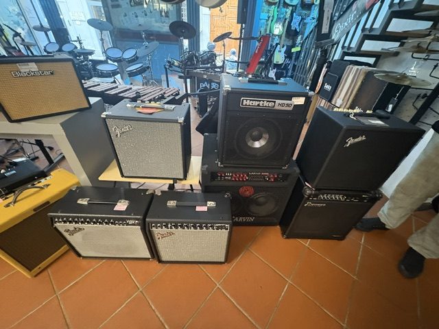 Guitar amplifiers stacked on a terracotta tiled floor, drums and keyboards behind