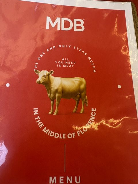 Red MDB steakhouse menu with a gold bull illustration lying on a table