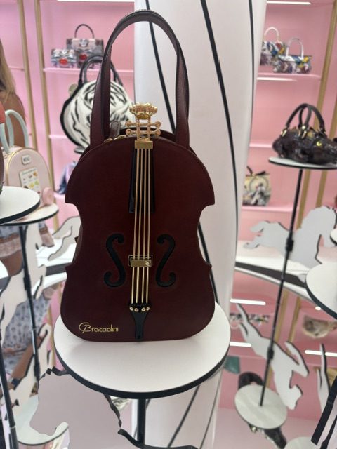 Violin-shaped handbag on a display stand in a pink shop window with other bags