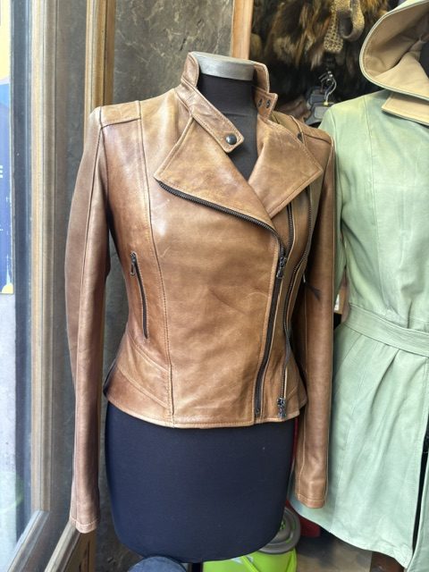 Tan leather jacket on a mannequin in a shop window beside a pale green garment