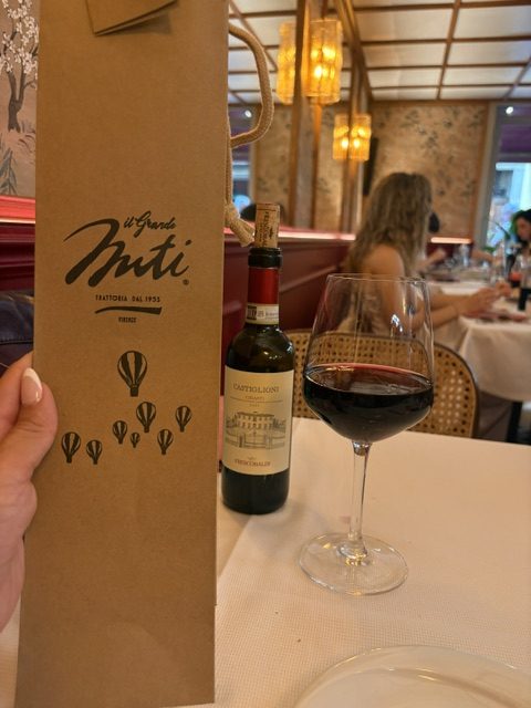 Il Grande Nuti paper menu held up beside a Chianti bottle and glass of red wine on a white tablecloth