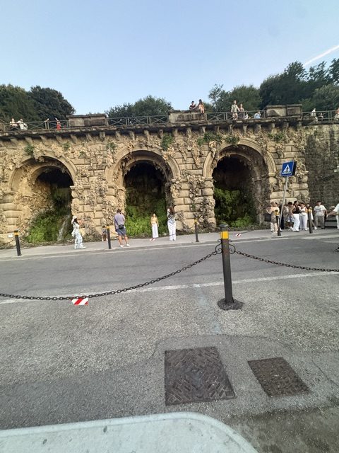 Stone arched retaining wall built into a hillside beside a roadway, greenery above