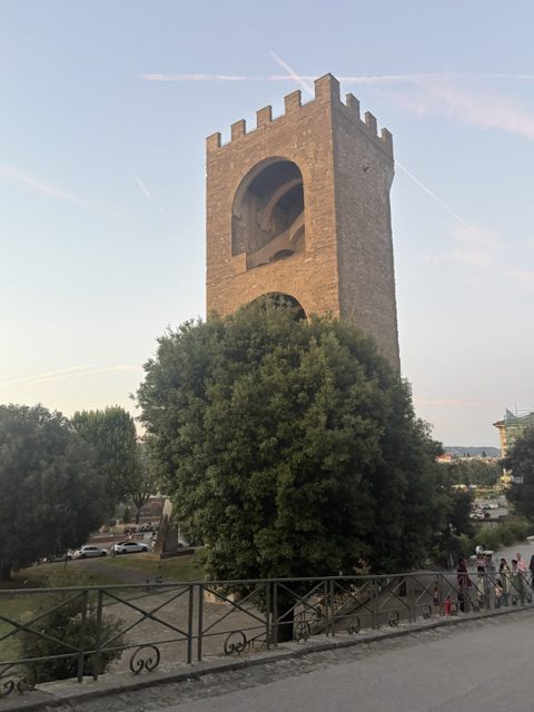 Tall crenellated brick tower rising above trees against a pale evening sky