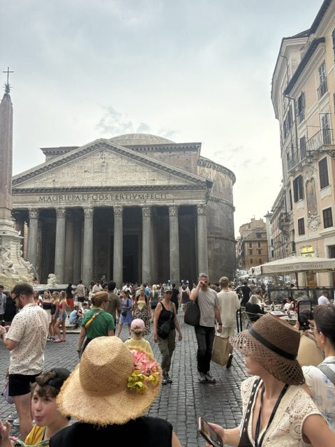 Pantheon portico, granite columns and pediment, dense crowd in the piazza, straw hats in the foreground