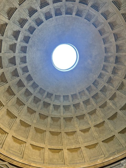 Coffered concrete dome of the Pantheon seen from directly below, open oculus of white daylight at the center