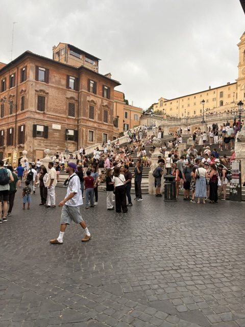 The Spanish Steps crowded with people, ochre buildings, wide cobbled piazza in the foreground