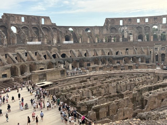 Colosseum interior, tiers of arches, the exposed underground hypogeum where the floor once was, crowds on the walkway