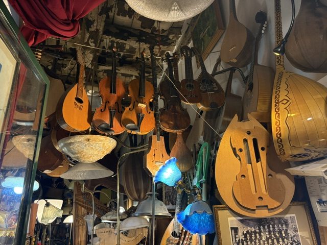 Shop window and interior crowded with hanging mandolins, violins, lutes and stained glass lamps